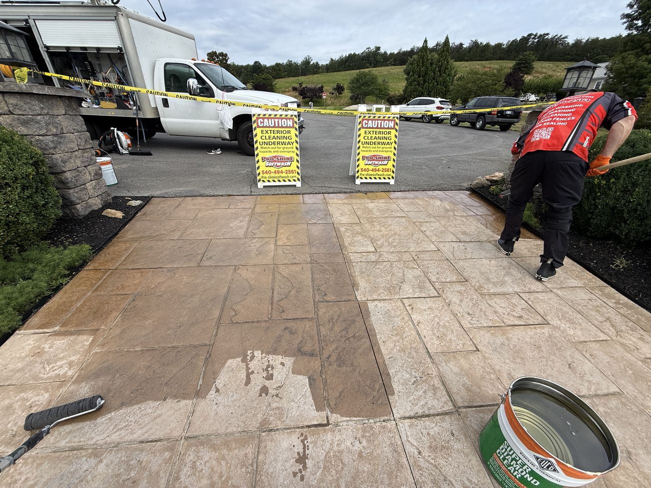 Pro-Shine Softwash crew applying decorative concrete sealer with caution signage and equipment on site